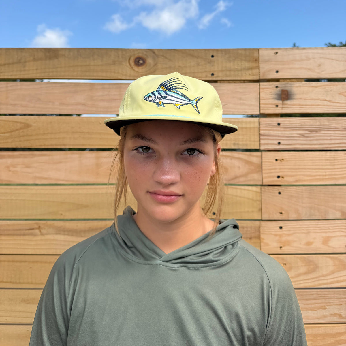 Salt SQD Coastal Icons Cap in Roosterfish, worn by a girl outdoors, showing front view with roosterfish logo and rope brim