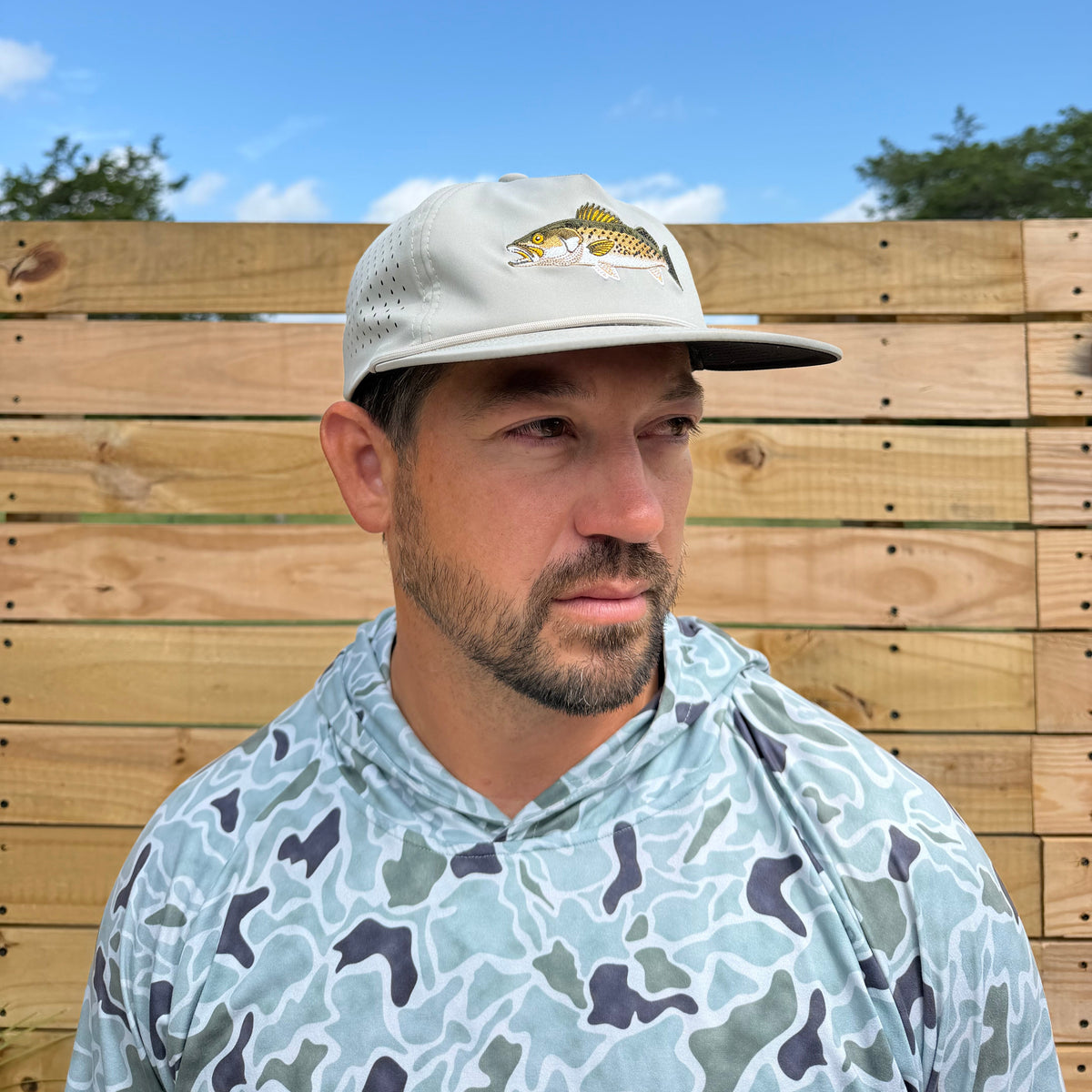 Salt SQD Coastal Icons Cap in Speckled Trout, worn by a man outdoors, showing the front view with speckled trout logo 