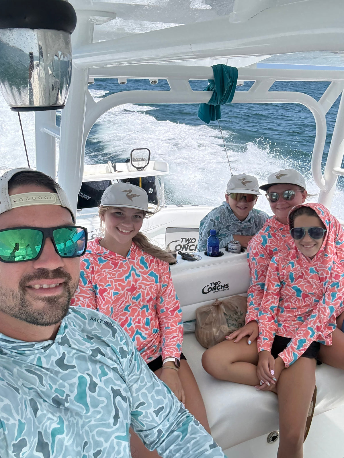 Family posing on a boat with ocean waves behind them, wearing matching coral and blue patterned shirts