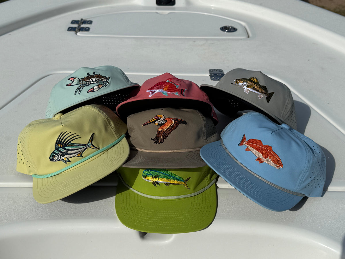 Six colorful baseball caps with embroidered fish and wildlife designs arranged on a light gray boat deck
