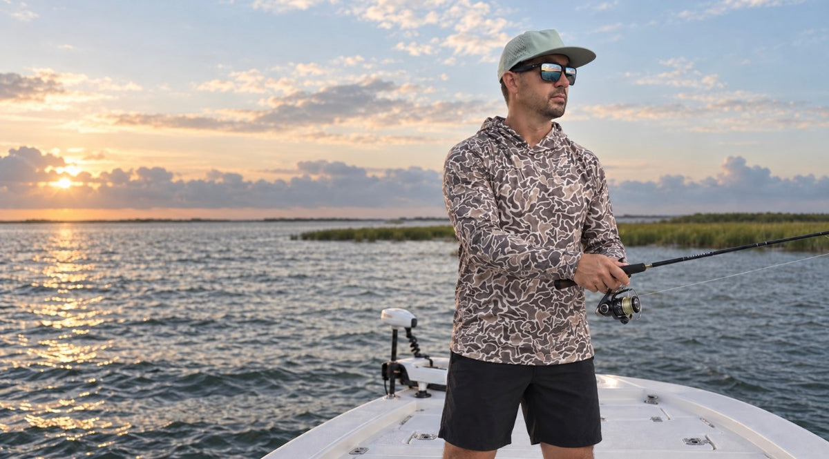 Angler wearing a patterned long sleeve shirt, cap and sunglasses while casting from a boat at sunset